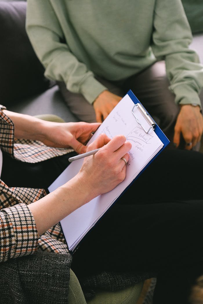 Close-up of a therapist taking notes during a session, focusing on the clipboard and pen.